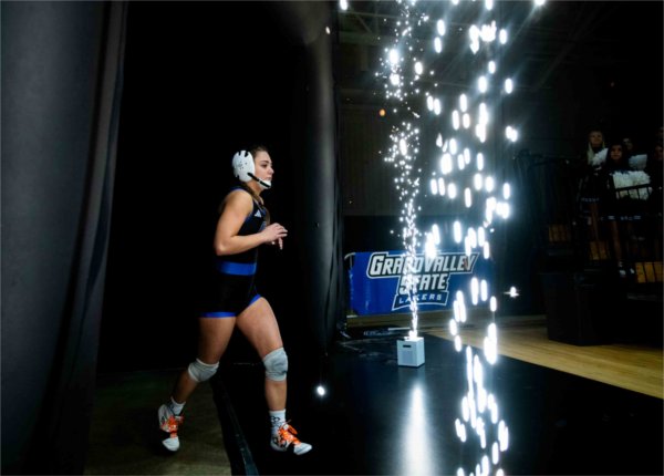    A member of the Women's Wrestling team runs past festive sparks while entering the arena.