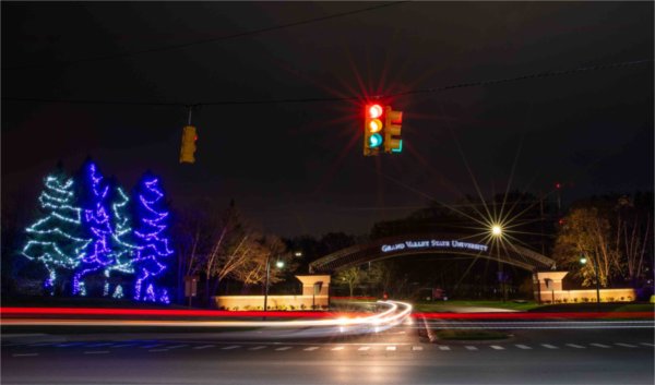 Holiday lights decorate the entrance to campus as traffic lights are blurred with a long camera exposure.