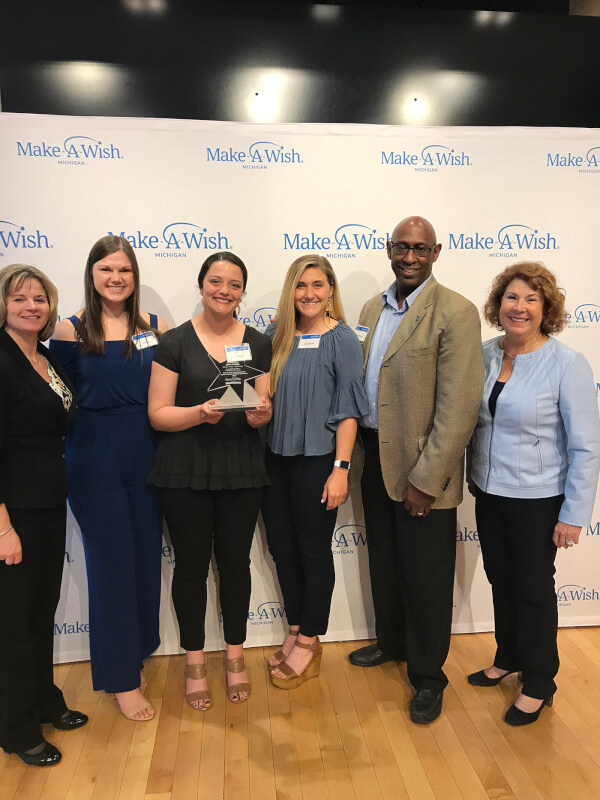 six people standing in front of Make-A-Wish Michigan backdrop