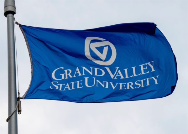 A blue flag flies while on a flagpole. It contains the words Grand Valley State University and the university's logo.