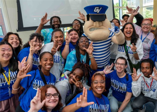  Students hold up a college hand signal as they surround the mascot.