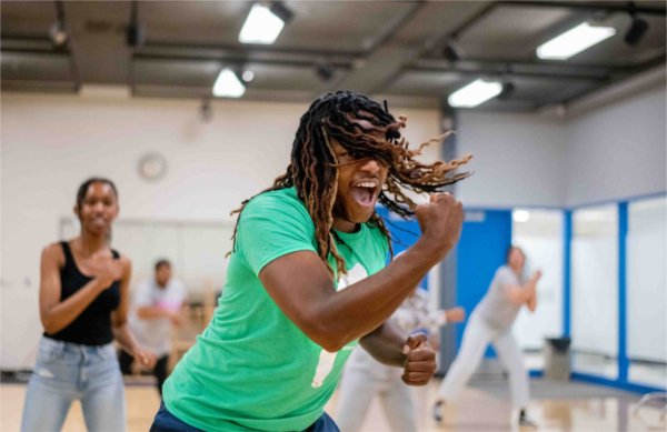  A person wearing a green shirt intently leads a dance routine with their hair swinging and fist clenched.