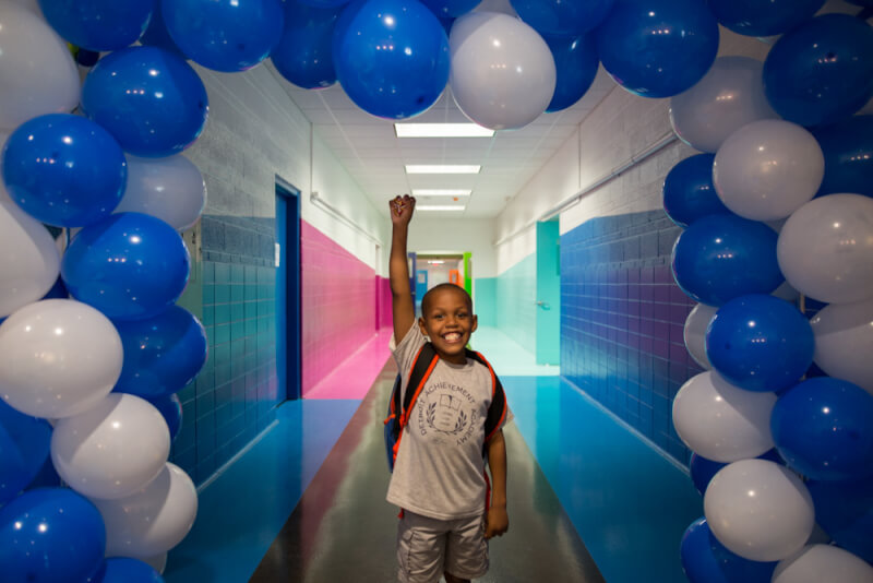 A student in a backpack stands underneath a bunch of balloons at the Detroit Achievement Academy.