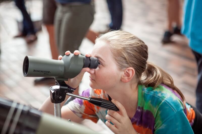 A photo of a girl interacting with a telescope.
