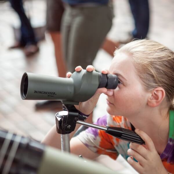 A photo of a girl interacting with a telescope.