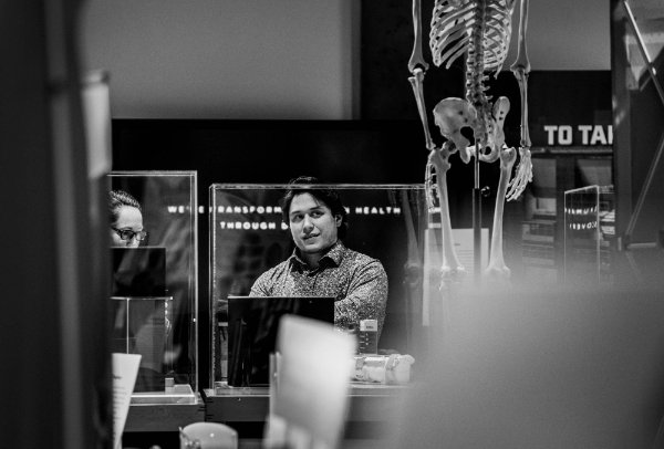 black and white photo of a man looking at a museum exhibit, a skeleton is in foreground