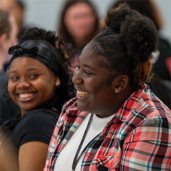 Two girls laugh as they listen to a speaker.