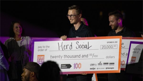 Zachary DeBruine, assistant professor of computing, poses for a photo with a large check after his Herd Social project was selected as one of the top 10 projects at Start Garden's Demo Day. 