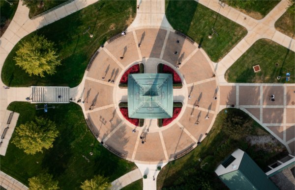 A drone photo looking straight down on the carillon tower of a campus community as students walk past. 