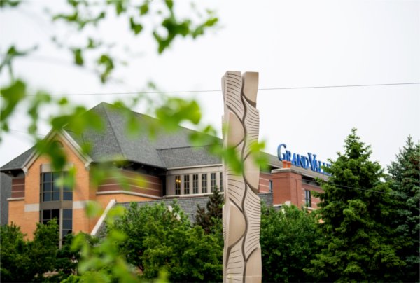 A stone sculpture with curving lines is in the foreground. A building is in the background.