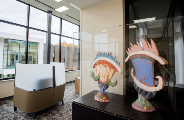 Two small, colorful sculptures sit on a table next to a window.