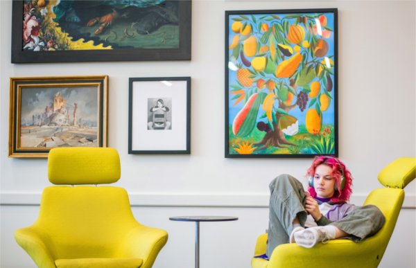 A person wearing headphones sits in a yellow chair. Several pieces of art on the wall in the background.