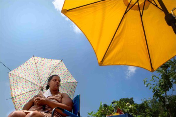  A person sits under an umbrella for shade while another yellow umbrella is nearby.