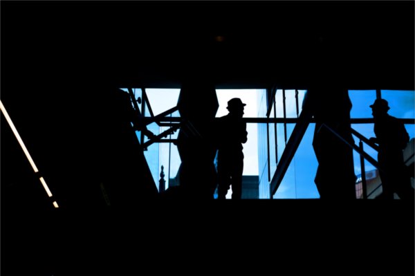   A person wearing a hat is silhouetted against a blue window. 