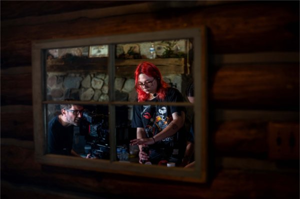  A person uses a movie camera on set of a film production while a person with bright red hair is seen reflected in a mirror. 