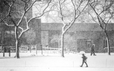 People walk across a snowy campus. One person is carrying an umbrella.