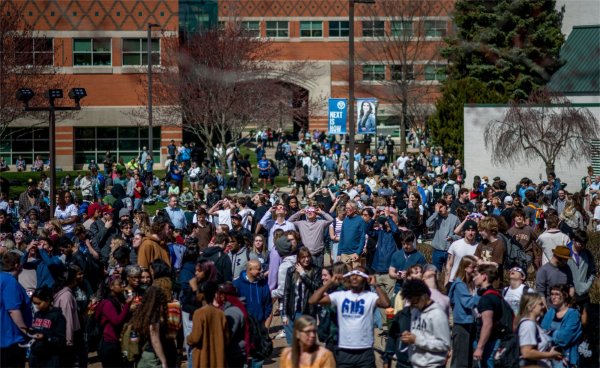 A large group of people gathers to use special glasses to observe the solar eclipse.