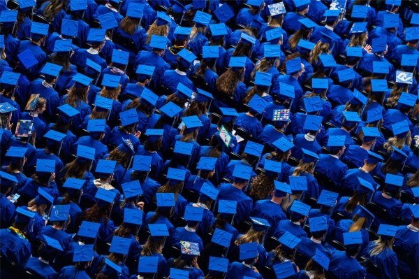 A large group of seated people wearing blue graduation caps are seen from above.