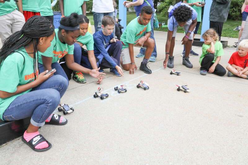 Campers racing their solar-powered cars under the Transformational Link sculpture.