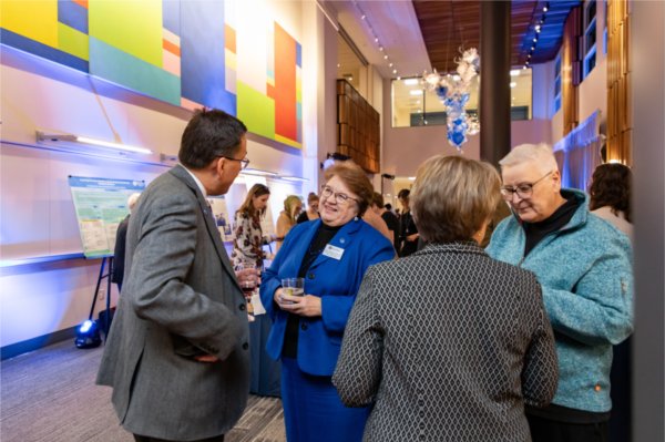 four people talking in pairs at reception, colorful artwork and posters presentations in the background