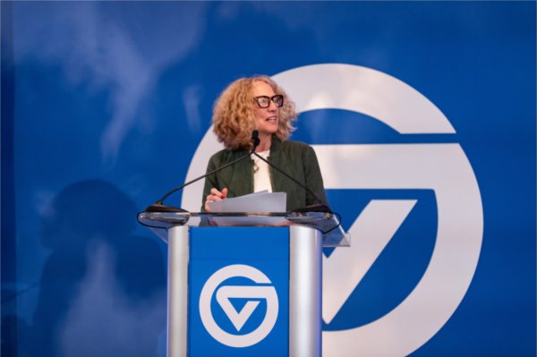 Jennifer Drake at the podium with large circle GV on blue banner in background