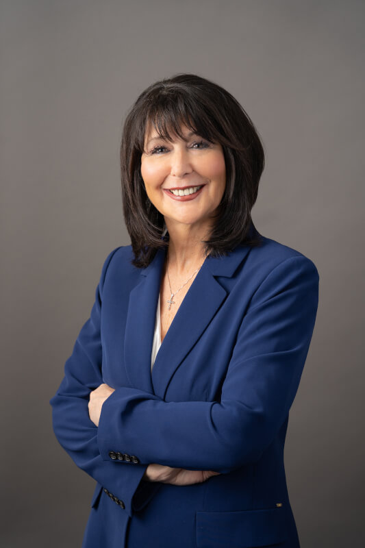 A portrait of Philomena Mantella. She is standing with arms crossed, and is wearing a dark blue jacket.