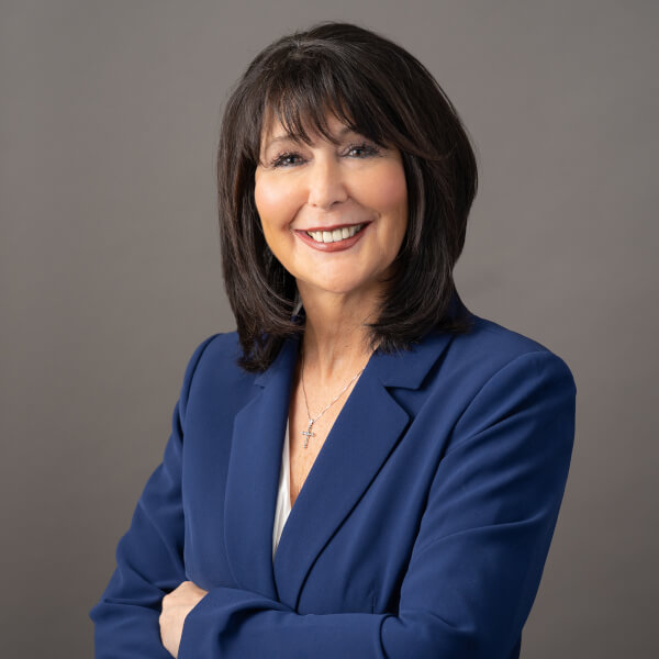 A portrait of Philomena Mantella. She is standing with arms crossed, and is wearing a dark blue jacket.