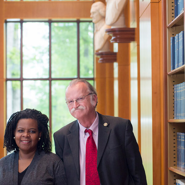 Annette Gordon Reed and Peter Onuf stand, smiling, side-by-side in a room with books on shelves on the right wall, There is a window in the background.