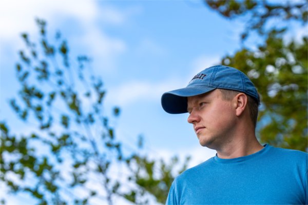 A person wearing a Grand Valley cap looks off into the distance. Trees are in the background.