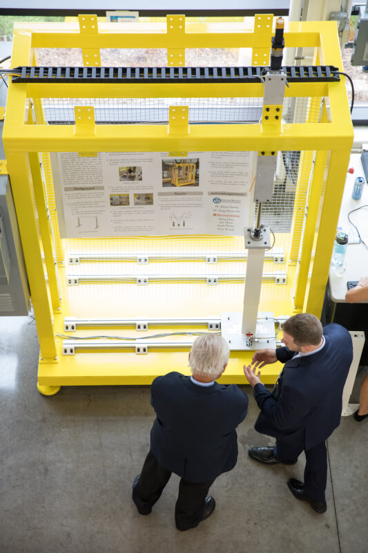  Two men standing near a yellow robotic cube