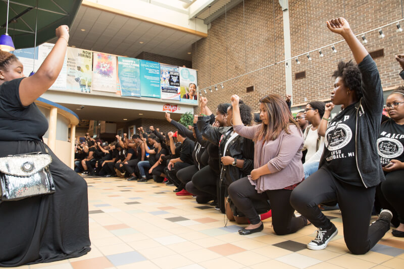 Photos by Amanda Pitts.  Students kneel with fists raised in the Kirkhof Center prior to holding a justice rally at the Cook Carillon Tower. Antoinette Jackson, NAACP chapter president, is at left.