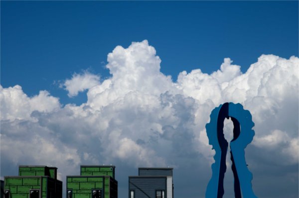  A blue art sculpture is seen in front of large puffy white clouds and a blue sky. 