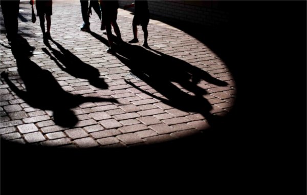  Shadows of children and parents make shapes on a brick walkway.