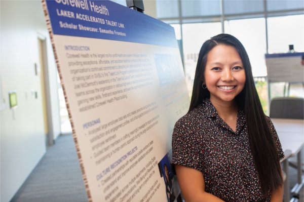 A person smiles while standing in front of a poster board. The words Corewell Health and Laker Accelerated Talent Link and Scholar showcase: Samantha Frondoso are visible.