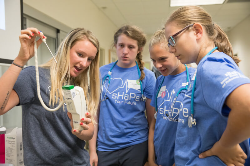 A Grand Valley nursing student (left) teaches campers how to measure vital signs