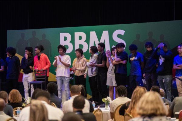 a group of students stands on stage in front of banner, BBMS