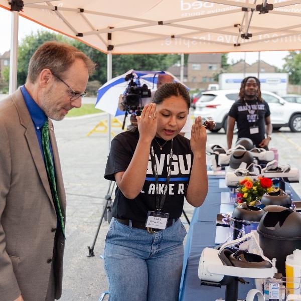 A GVSU student Erika Govea-Garcia explains how to use the VR headset to Mary Free Bed CEO Kent Riddle.