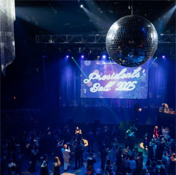 An above shot of a room full of Lakers dancing. A sign hanging reads Presidents� Ball 2025. A large silver disco ball hangs from the ceiling.