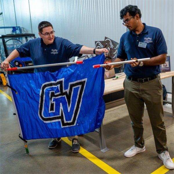 two men stand behind a GV flag while placing a pole through the flag