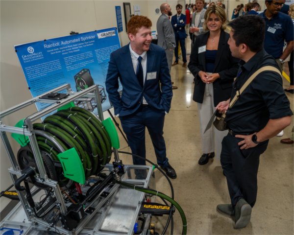 three people stand next to what looks like a large garden hose at Senior Project Day in the Innovation Design Center