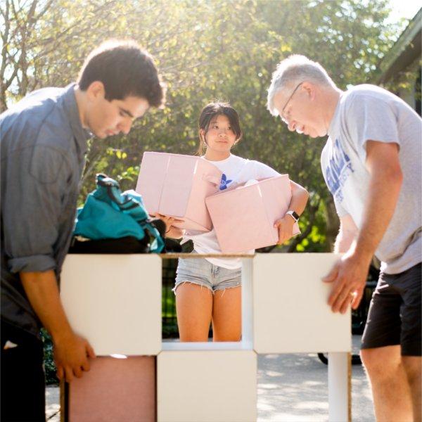 Two people stand on either side of a multi-tiered storage container while another person carrying bins stands behind them.