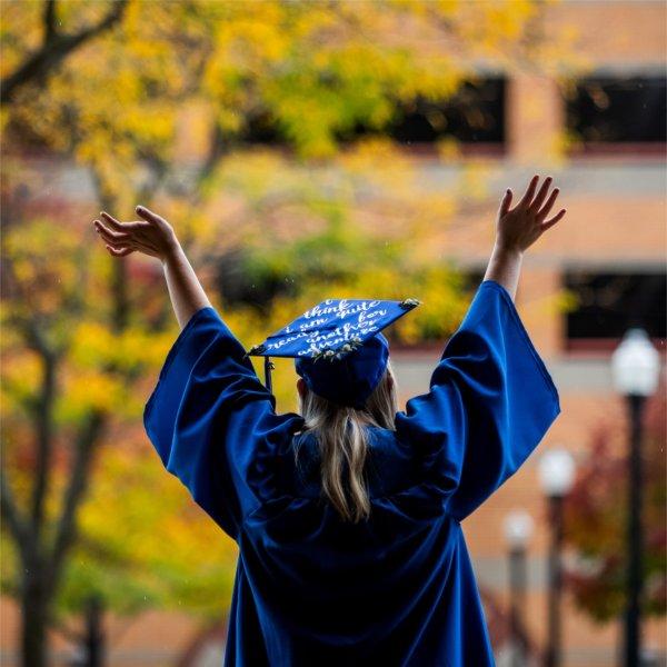 Graduate posing in cap and gown raises her arms in celebration.