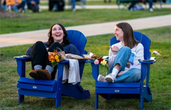  Two college students laugh together as they sit in blue Adirondack chairs.