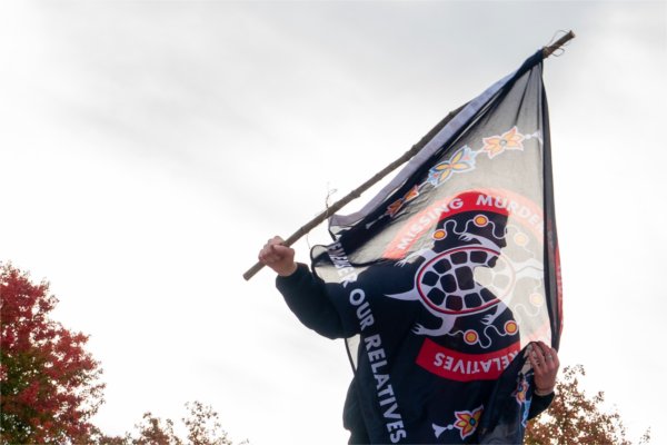  A student is silhouetted through a red and black flag they are carrying. 