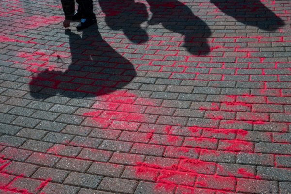  Shadows of students crouched over are cast on bricks with red sand being poured in the cracks. 