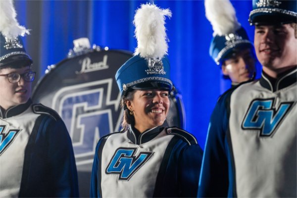  A college student wearing a band uniform with the letters GV on the front smiles with others. 