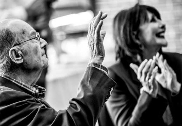 Two people look up and wave and clap as students are introduced as scholarship recipients.  