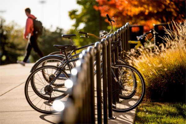  A student wearing a backpack walks past a row of bicycles in a bike rack. 