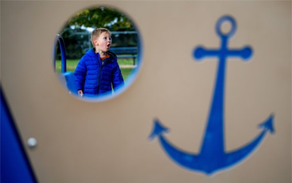  A small child is seen through a circle of playground equipment with a blue anchor on the side. 