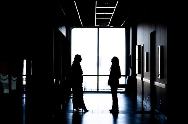  Two people are silhouetted against a window in a long hallway of an academic building. 